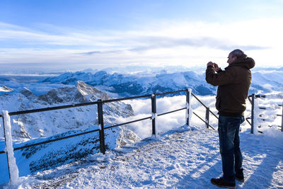 Side view of man standing by snowcapped mountains against cloudy sky