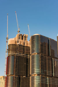 Low angle view of crane by building against clear blue sky