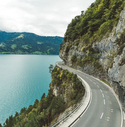 Empty road amidst mountain and lake against cloudy sky