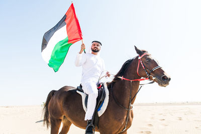 Low angle view of man with flag sitting on horse