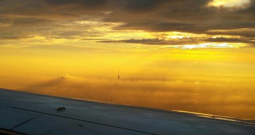 Cropped image of aircraft wing with fernsehturm amidst clouds