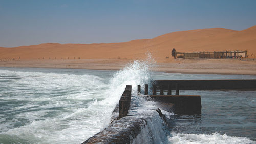 Waves splashing on shore against clear sky