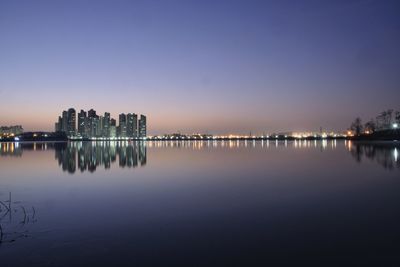 Illuminated buildings by lake against sky at dawn