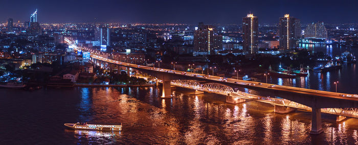 Illuminated bridge over river by buildings in city at night