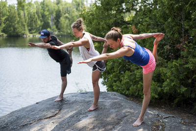 Friends stretching legs while practicing yoga on rock at lakeshore