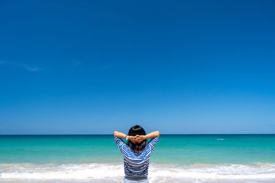 Rear view of woman standing at beach against blue sky