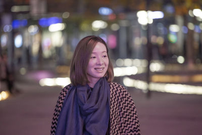 Smiling woman standing on illuminated street at night