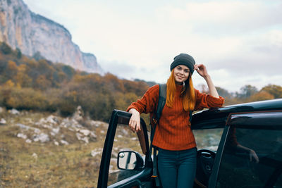 Young woman using phone while standing on car