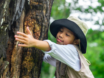Portrait of young woman standing by tree trunk
