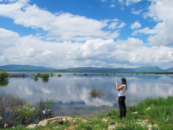 Full length of woman standing by lake against sky