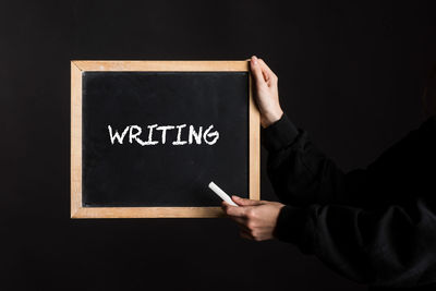 Midsection of man holding blackboard against black background