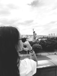 Rear view of woman photographing in city against sky