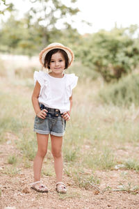 Smiling little kid girl 3-4 year old wearing stylish summer clothes and straw hat standing in park