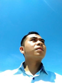 Low angle portrait of teenage boy against blue sky