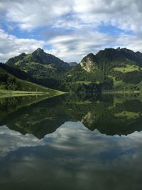 Scenic view of lake by mountains against cloudy sky