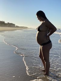 Woman standing on shore at beach against sky
