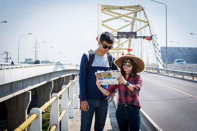 Couple reading map while standing on bridge in city