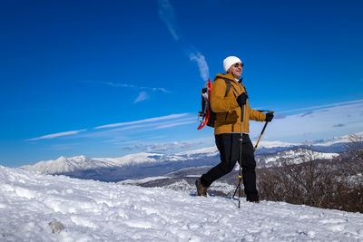 Full length of man skiing on snow covered landscape against blue sky