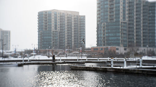 Modern buildings by river against sky in city