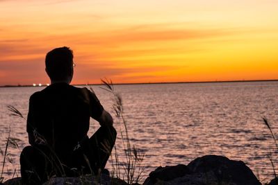 Rear view of man looking at sea against orange sky