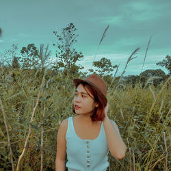 Young woman looking away while standing on field against sky