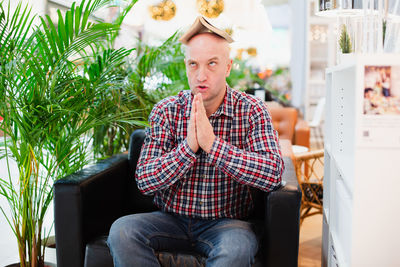 Man with hands clasped sitting on sofa having book on head