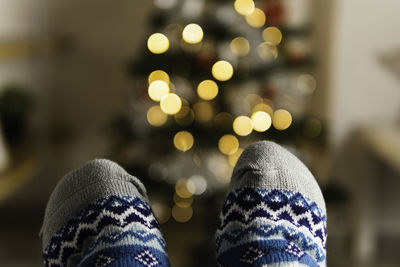 Close up of feet wearing warm christmas socks with illuminated christmas tree on the back ground