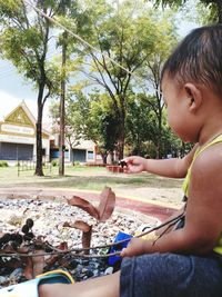 Side view of boy sitting on plant against trees