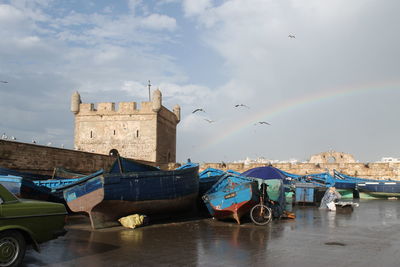 Boats moored on shore by fort during low tide against sky