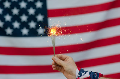 Cropped hand of person holding illuminated sparklers against american flag