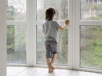 Boy looks outdoors through window with raindrops. kid stays alone at home. coronavirus covid-19.