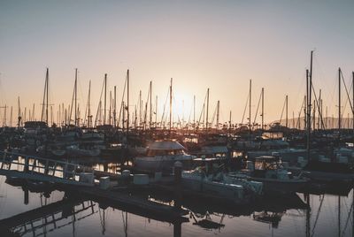 Sailboats moored in harbor at sunset