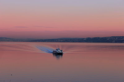 Boat sailing on sea against orange sky