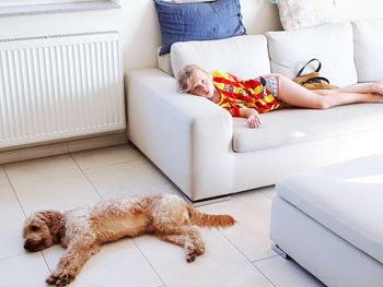 Portrait of girl relaxing by dog on sofa in living room at home