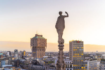 Statue from the top of the cathedral in milan with the torre velasca in the background before the sunset