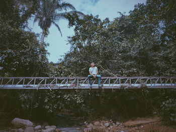 Woman standing on footbridge against trees