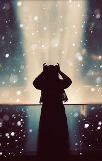 Silhouette woman standing in snow against sky at night