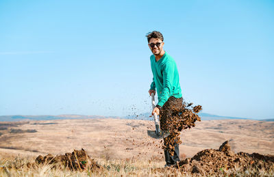 Young man with shovel digging on land against clear sky
