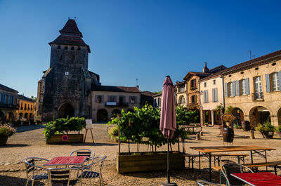 Chairs and table by buildings against clear blue sky