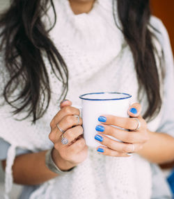 Close view of the hands of a young woman holding a white enameled mug with coffee or tea