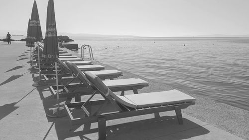 Deck chairs on sea against clear sky