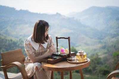 Woman sitting on chair at table against mountain range