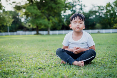 Boy with eyes closed sitting on grassy field