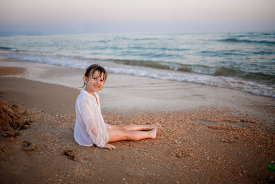 Woman sitting on shore at beach against sky