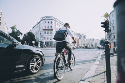 Full length of male entrepreneur riding bicycle on road in city against sky