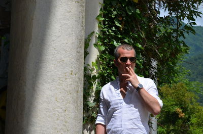 Portrait of man wearing sunglasses standing against plants