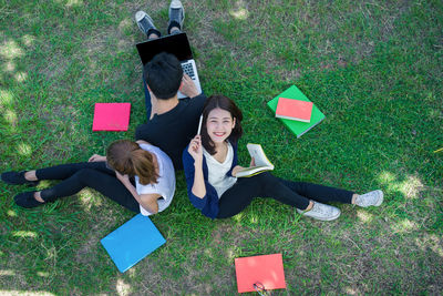 Portrait of happy girl with book sitting by friends on grassy field