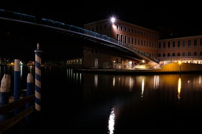 Illuminated bridge over river by buildings at night