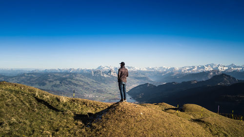 Rear view of man standing on mountain against clear sky