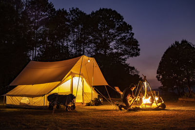 People relaxing on field by trees against sky at night